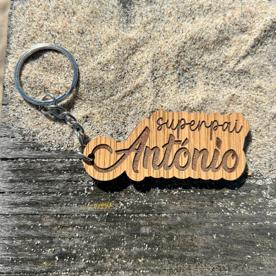Porta-chaves de madeira com gravação superpai António sobre areia e madeira