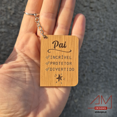 Chaveiro de madeira com texto em português sobre pai, segurado numa mão com fundo cinzento