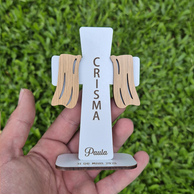 Figura de cruz branca com detalhes em madeira clara e texto CRISMA, Paula, 31 DE MAIO 2026