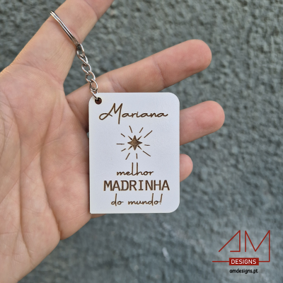 Chaveiro branco com texto gravado a laser em castanho segurado por mão, fundo cinza