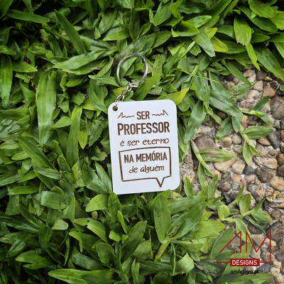 Chaveiro branco com texto sobre folhas verdes e pedras, logótipo AM DESIGNS