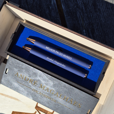 Caixa de madeira com duas canetas azuis personalizadas e embalagem cinzenta com texto dourado.