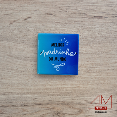 Quadrado azul com texto 'MELHOR padrinho DO MUNDO' sobre madeira clara
