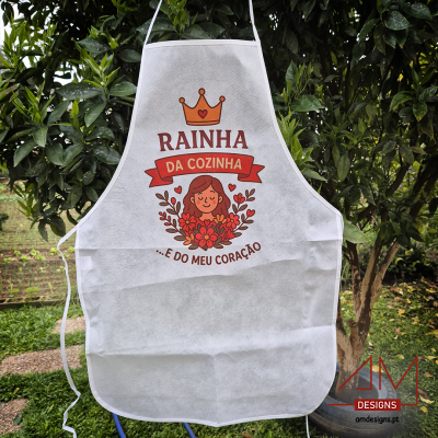 Avental branco com mensagem 'RAINHA DA COZINHA E DO MEU CORAÇÃO' e ilustração colorida, pendurado ao ar livre