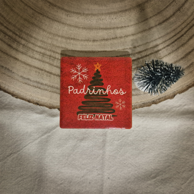 Quadrado cerâmico vermelho decorativo com texto de Natal e mini árvore ao lado