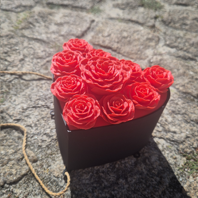 Caixa preta em forma de coração com rosas vermelhas artificiais em superfície de pedra