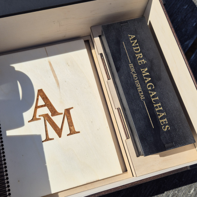 Caixa de madeira clara com letras gravadas e caixa preta com texto dourado dentro