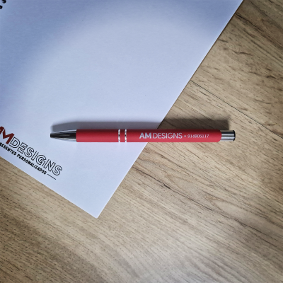 Caneta vermelha com texto branco sobre papel branco com logótipo sobre mesa de madeira clara