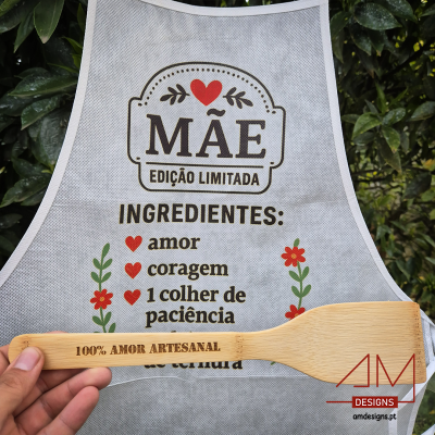 Avental branco com texto e colher de madeira gravada segurados em ambiente exterior com vegetação