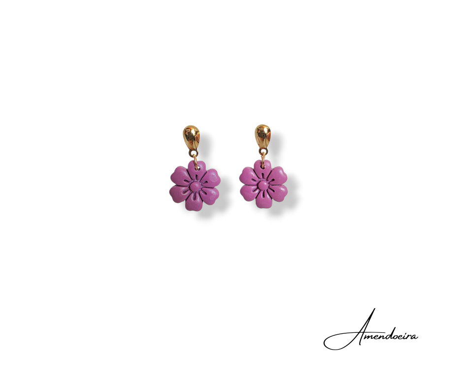 Brincos Camélia - Lilás Brincos dourados com pendentes rosa em forma de flor sobre fundo branco