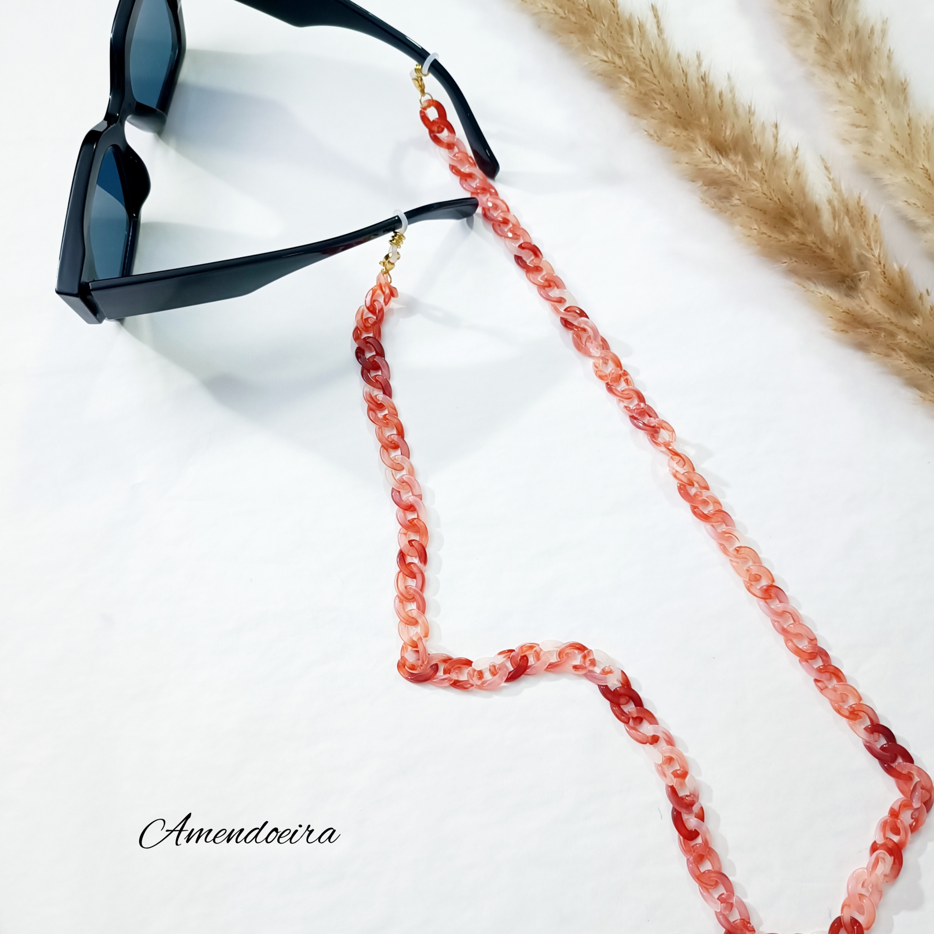 Fita para óculos - Acrílico Moccasin malva Óculos de sol preto com corrente de acrílico vermelho-rosa sobre superfície branca