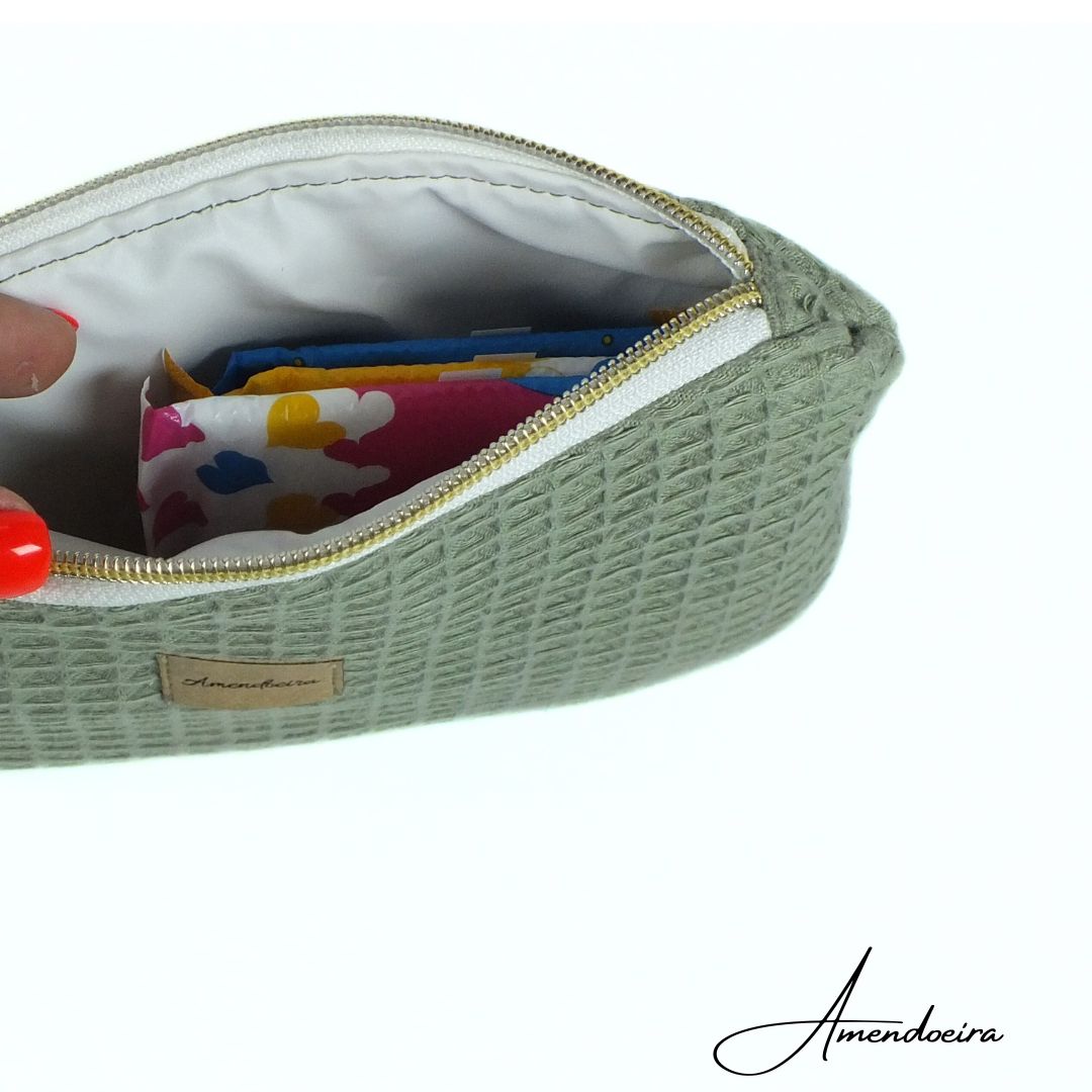 Liam waffle verde seco- bolsa nécessaire Estojo verde com padrão colmeia e fecho dourado aberto, mostrando interior e objetos coloridos dentro