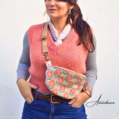 Bolsa tipo pochete em tecido floral com alça bege usada por mulher com colete rosa e camisa cinza