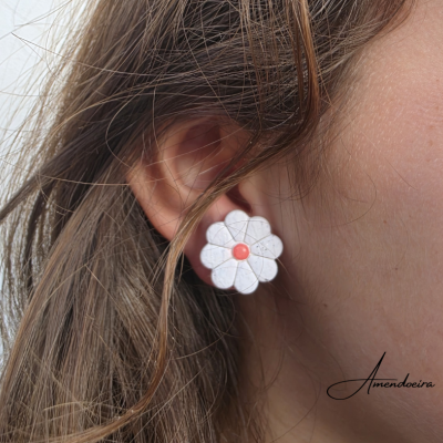 Brinco flor branco com centro laranja na orelha de uma pessoa