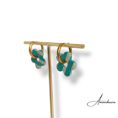 Brincos dourados com pendentes em forma de flor verde e branco num suporte dourado
