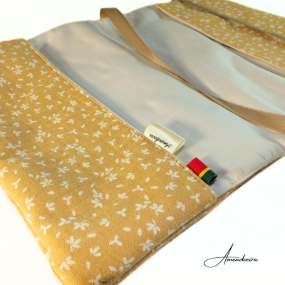 Estojo aberto amarelo com flores brancas e interior cinza, fita bege e etiqueta com texto