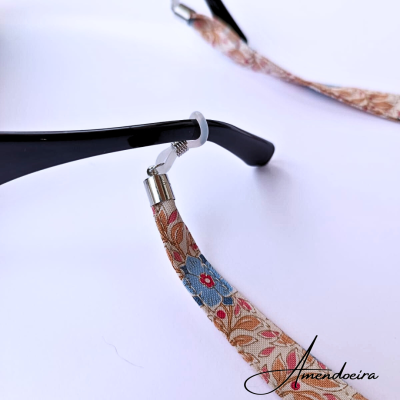 Cordão para óculos em tecido floral com acabamento metálico contra fundo branco
