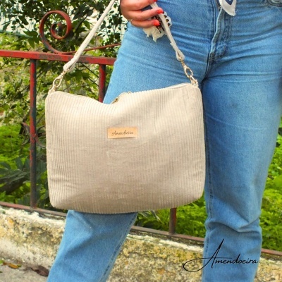 Mala bege com padrão riscado e alça regulável em corda num jardim