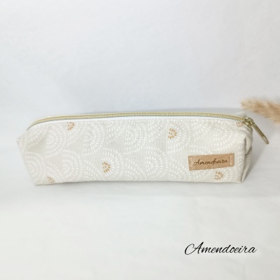 Estojo branco com padrão circular e fecho dourado com etiqueta Amendoeira