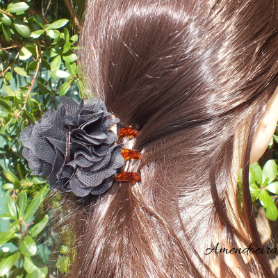 Presilha castanha com flor preta em cabelo castanho junto a plantas verdes