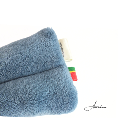 Toalha azul com etiquetas coloridas e texto Amendoeira no fundo branco