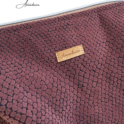 Pochete com padrão de pele de réptil castanho e etiqueta com texto Amendoeira