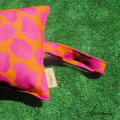 almofada rosa e laranja com padrão e alça sobre relva sintética verde