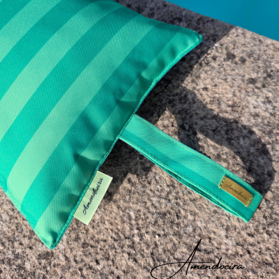 Almofada verde riscada sobre pedra junto a piscina com etiquetas Amendoeira