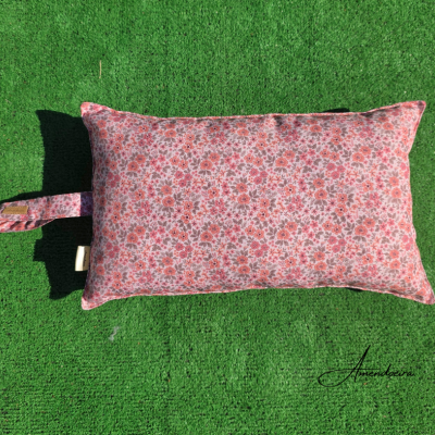 Almofada floral rosa retangular com alça lateral sobre fundo verde