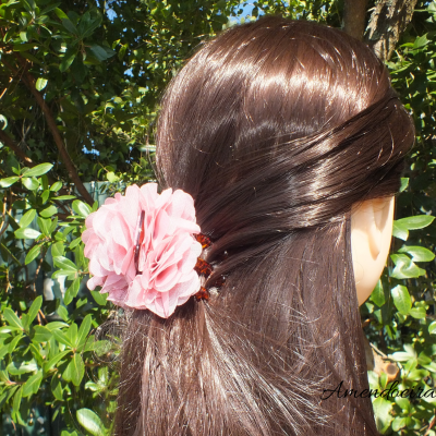 Presilha de cabelo com flor rosa em cabelo castanho escuro num cenário natural