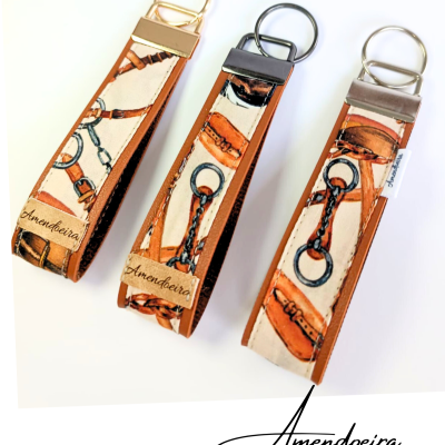 Três porta-chaves de tecido com padrão de arreios e pele castanha com argolas metálicas e etiqueta Amendoeira