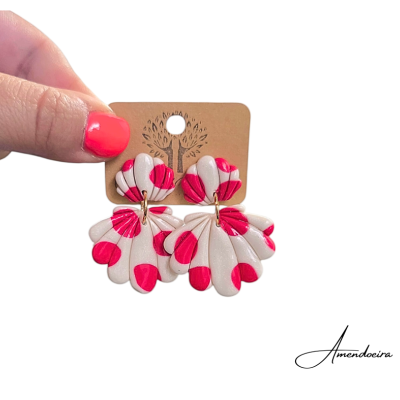 Brincos florais creme e rosa em suporte castanho segurado por mão com unhas pintadas de rosa