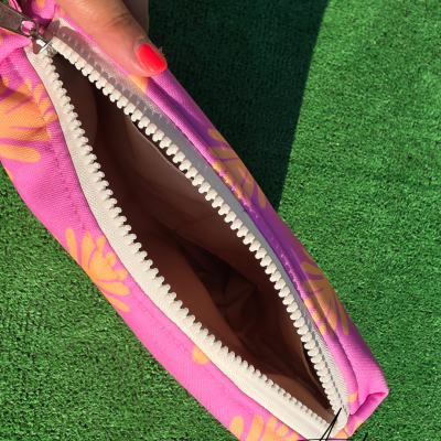 Bolsa rosa com padrão de folhas amarelas e fecho branco aberta sobre relva verde