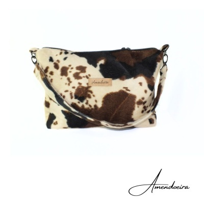 Mala tiracolo com padrão de pele de vaca em castanho, preto e branco e etiqueta Amendoeira