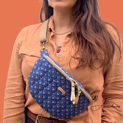 Bolsa pochete azul com padrão colorido e zíper bege usada sobre camisa bege.