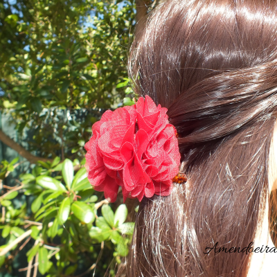 Presilha de cabelo vermelha em forma de flor numa pessoa com cabelo castanho claro e fundo de folhas verdes