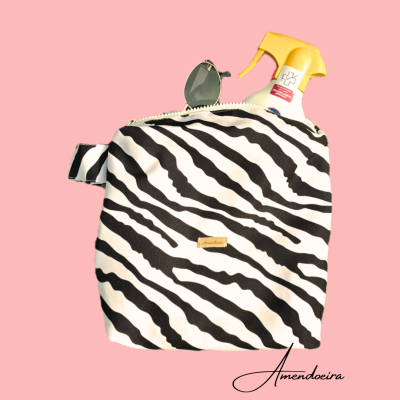 Bolsa com padrão zebra preto e branco com rótulo Amendoeira, spray amarelo e óculos