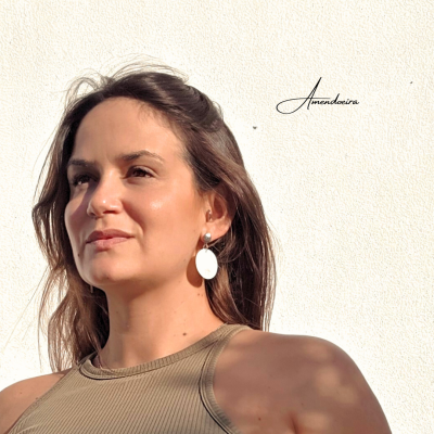 Mulher com brincos ovais brancos e top verde-oliva em fundo branco com texto Amendoeira