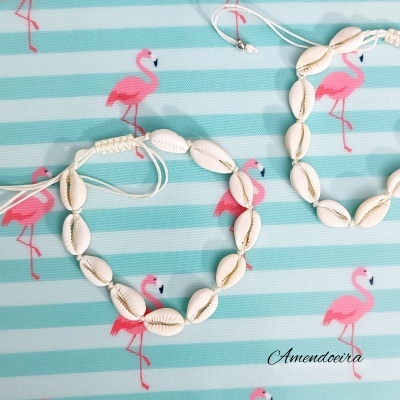 Pulseiras de conchas sobre tecido azul claro com flamingos cor-de-rosa