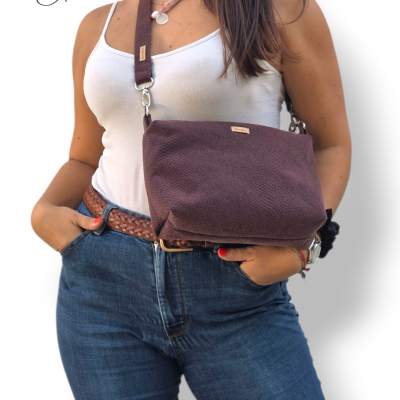 Mala castanha com textura tipo pele de cobra e alça larga castanha usada por mulher com jeans e t-shirt branca