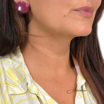 Mulher com brinco redondo roxo e camisa amarela com padrão branco