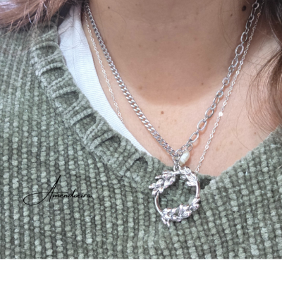 Colar feminino com correntes prateadas e pendente circular com folhas em fundo verde.