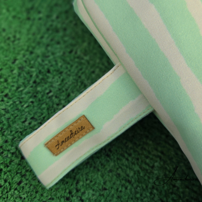 Almofada listrada verde-água e branca com etiqueta 'Lancheria' em superfície verde