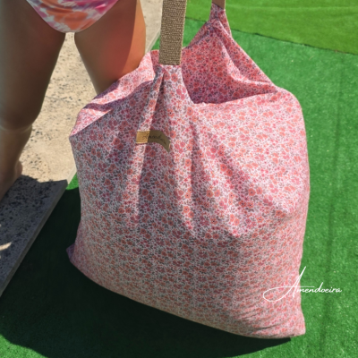 Saco de tecido floral rosa com alças castanhas junto a relva e piscina