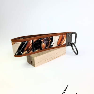 Porta-chaves de tecido estampado em tons castanhos com anel metálico sobre bloco de madeira