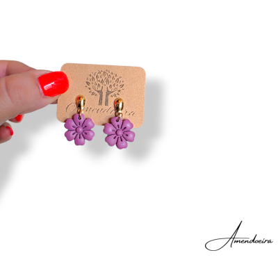 Brincos de flores roxas com acabamento dourado numa placa com logótipo Amendoeira