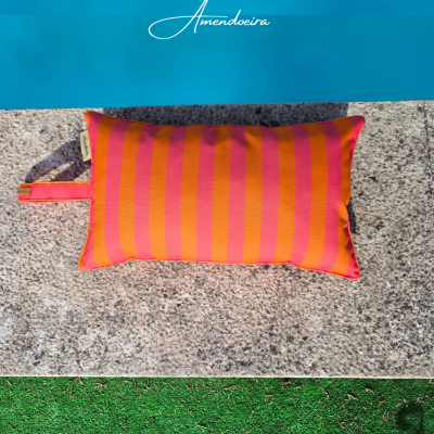 Almofada laranja e rosa com riscas junto a piscina e relva artificial