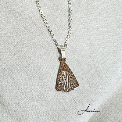 Colar prateado com pendente triangular de filigrana sobre tecido cinza claro