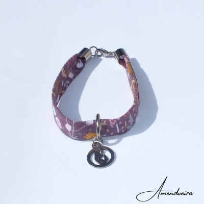 Pulseira de tecido floral roxa com pendente metálico sobre fundo branco