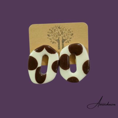 Brincos ovais castanhos e brancos com padrão de manchas sobre cartão com símbolo de árvore.